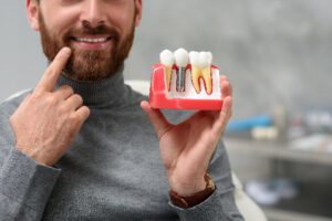 man holding up a model of a dental implant pointing to his mouth, showing where the implant would take root