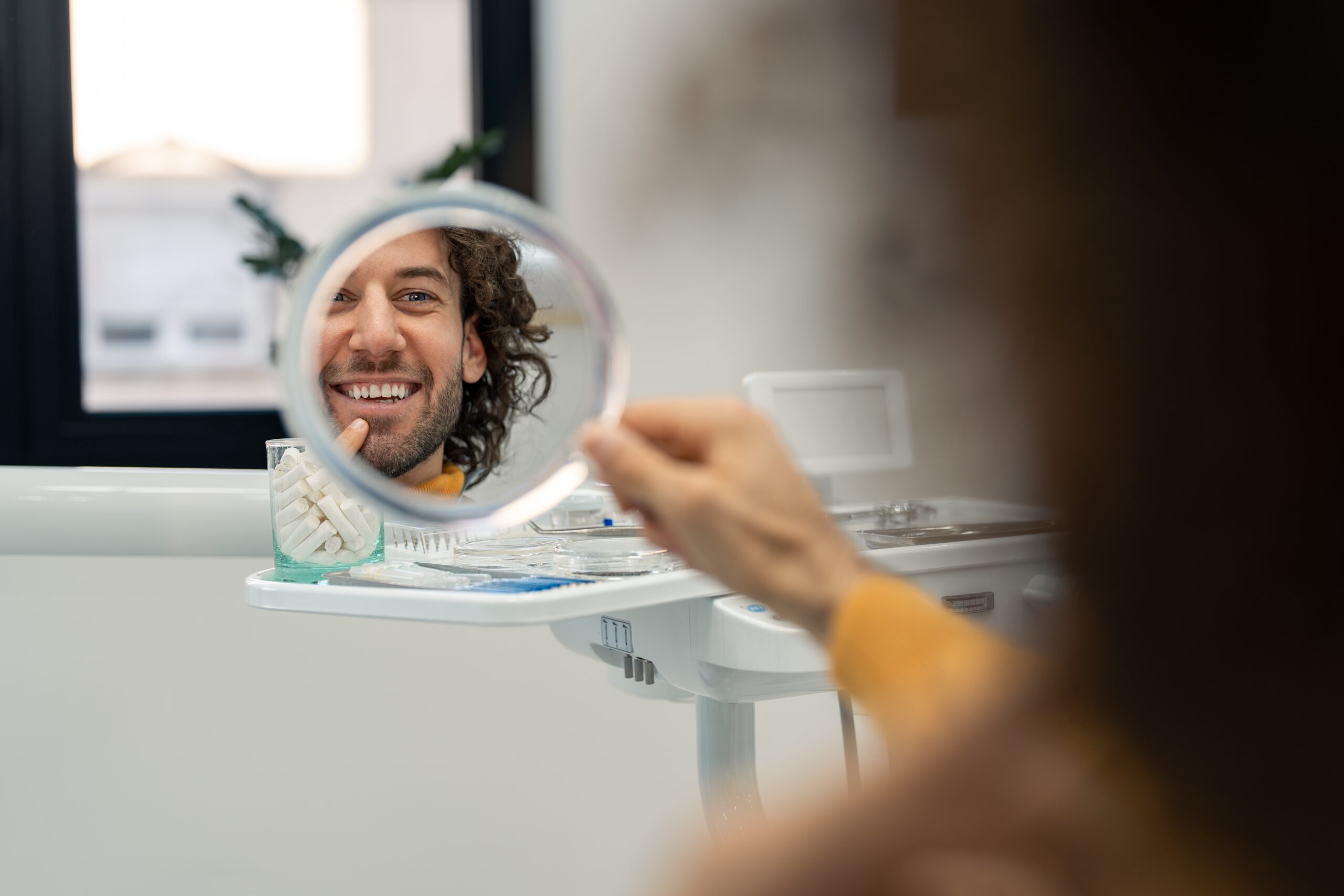 man smiling in a mirror, looking at his new dental implants
