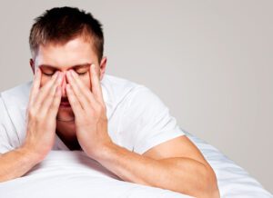 tired man sitting up in bed with his hands on his face, sleep apnea