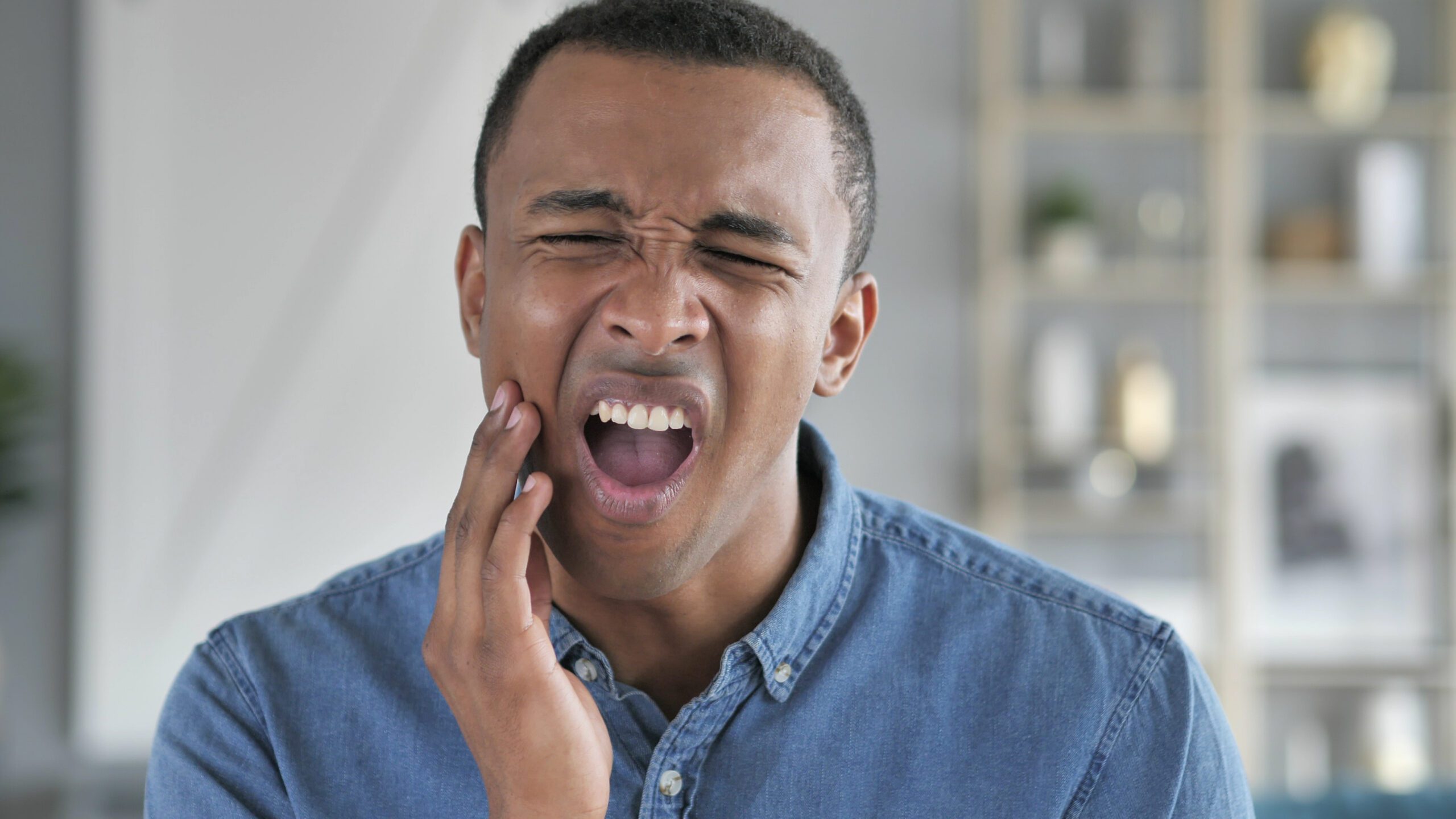 young man in a blue shirt holding his jaw, severe tooth pain or infection