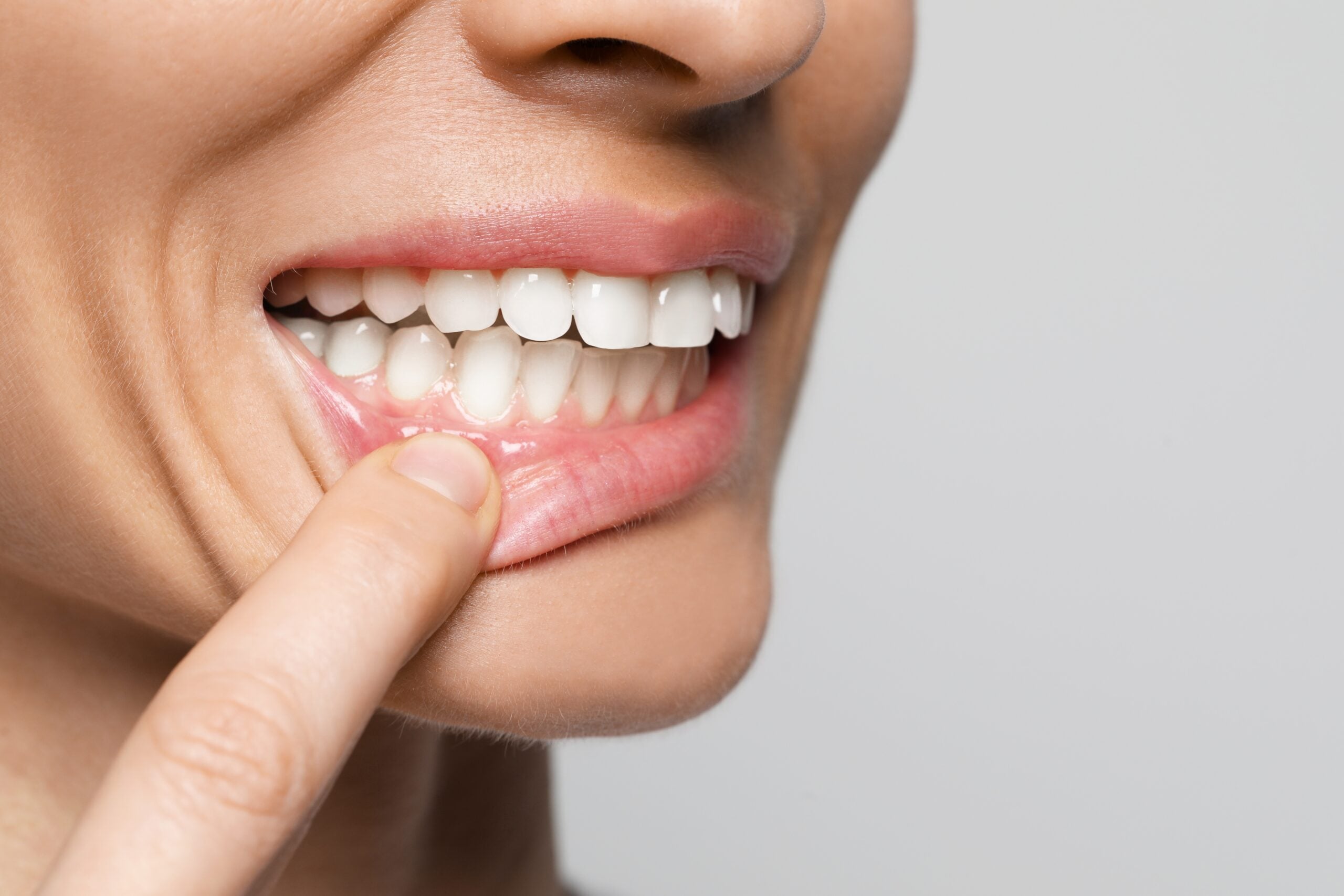 Woman showing healthy gums against a light background, in a closet